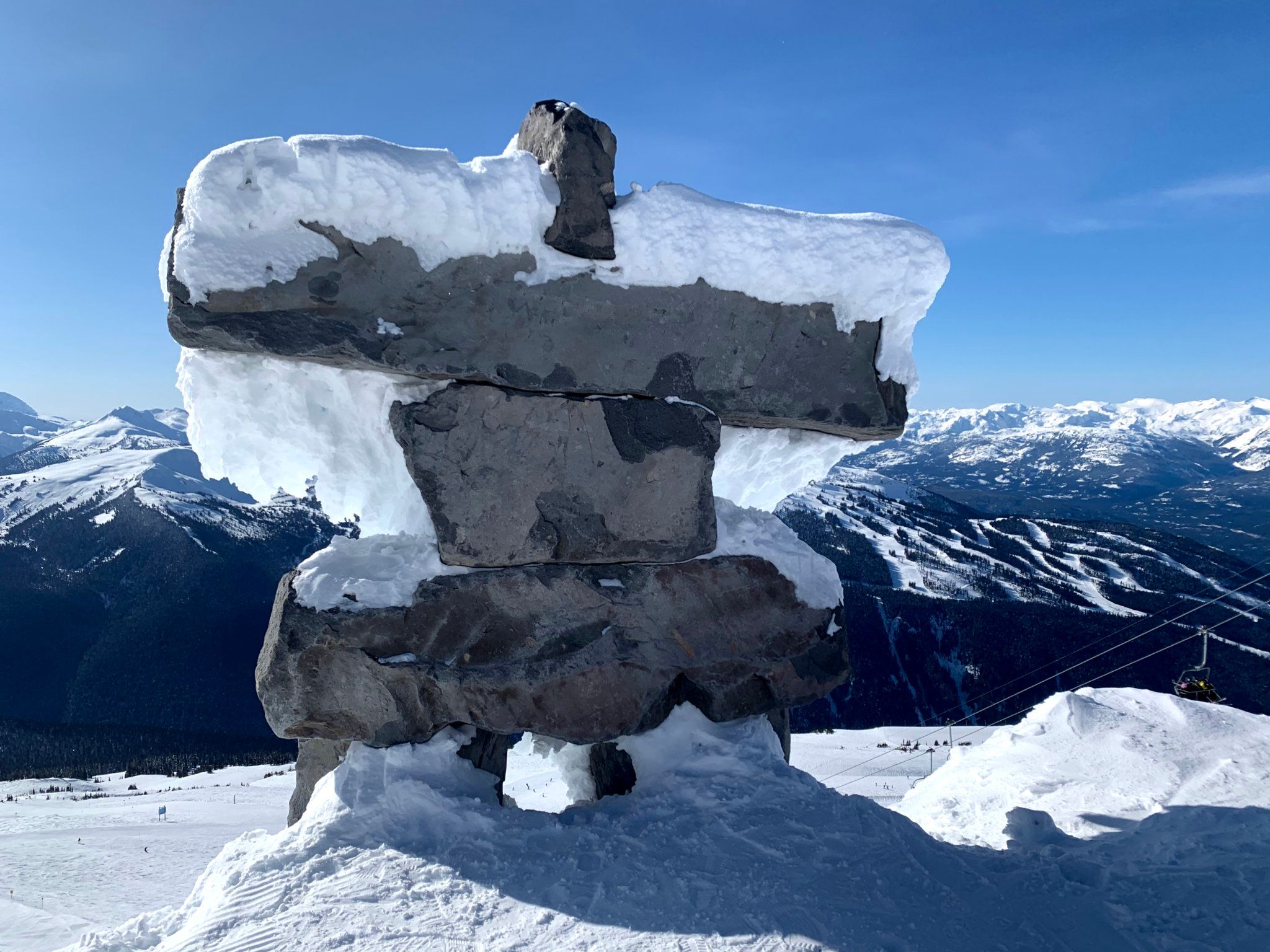 Stone inukshuk statue on Whistler Mountain with alpine peaks behind.