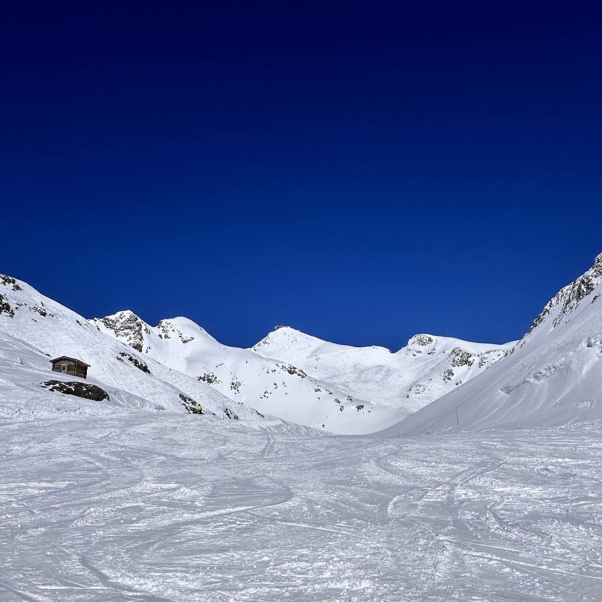 A wide open snow bowl on the Sarenne with a stone hut on the left and tracks running right across the face.