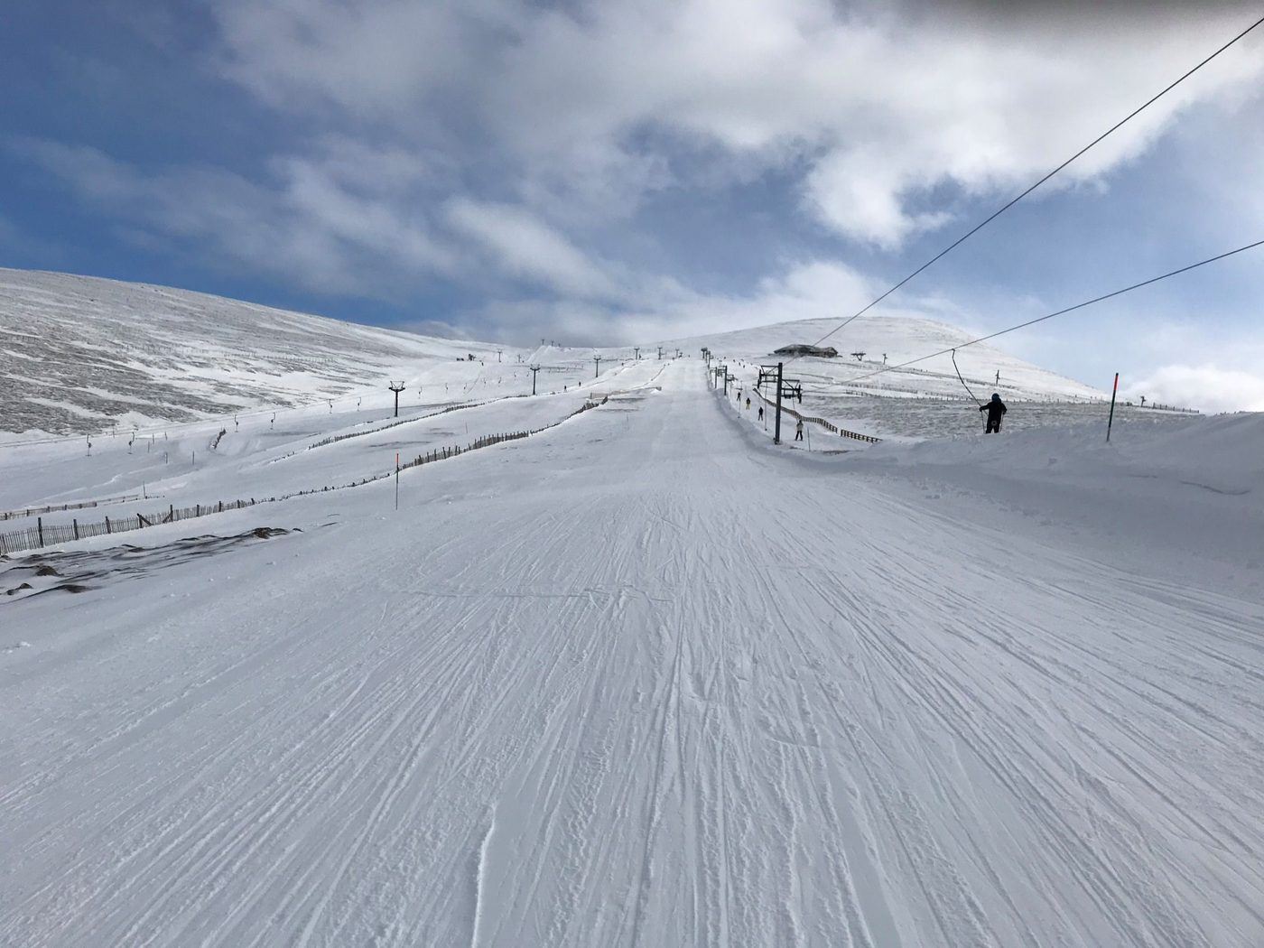 Skiers on the snow-covered pistes of Cairngorm Mountain ski area beside a drag lift under a blue Highland sky