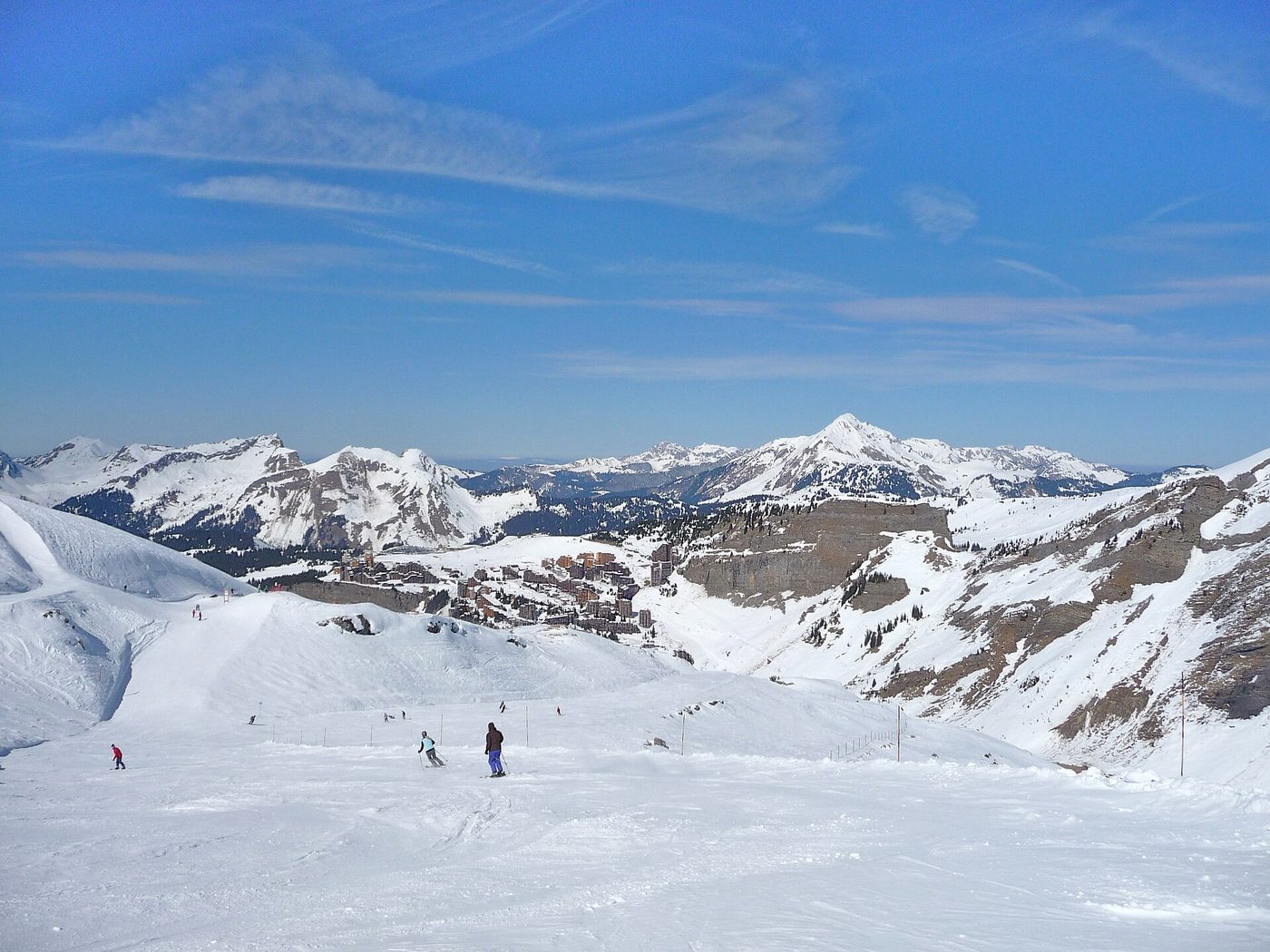 Skiers descending a wide, sunny piste above Avoriaz with the Portes du Soleil mountain panorama behind