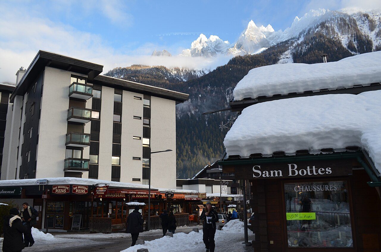 Snow-covered street in Chamonix town in winter with shops, skiers and the Aiguille peaks behind