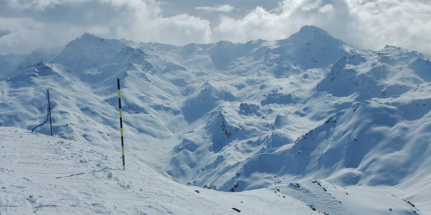 Dramatic snow-covered high-alpine terrain in the Les Trois Vallées ski area with steep faces and off-piste snowfields under a cloudy sky