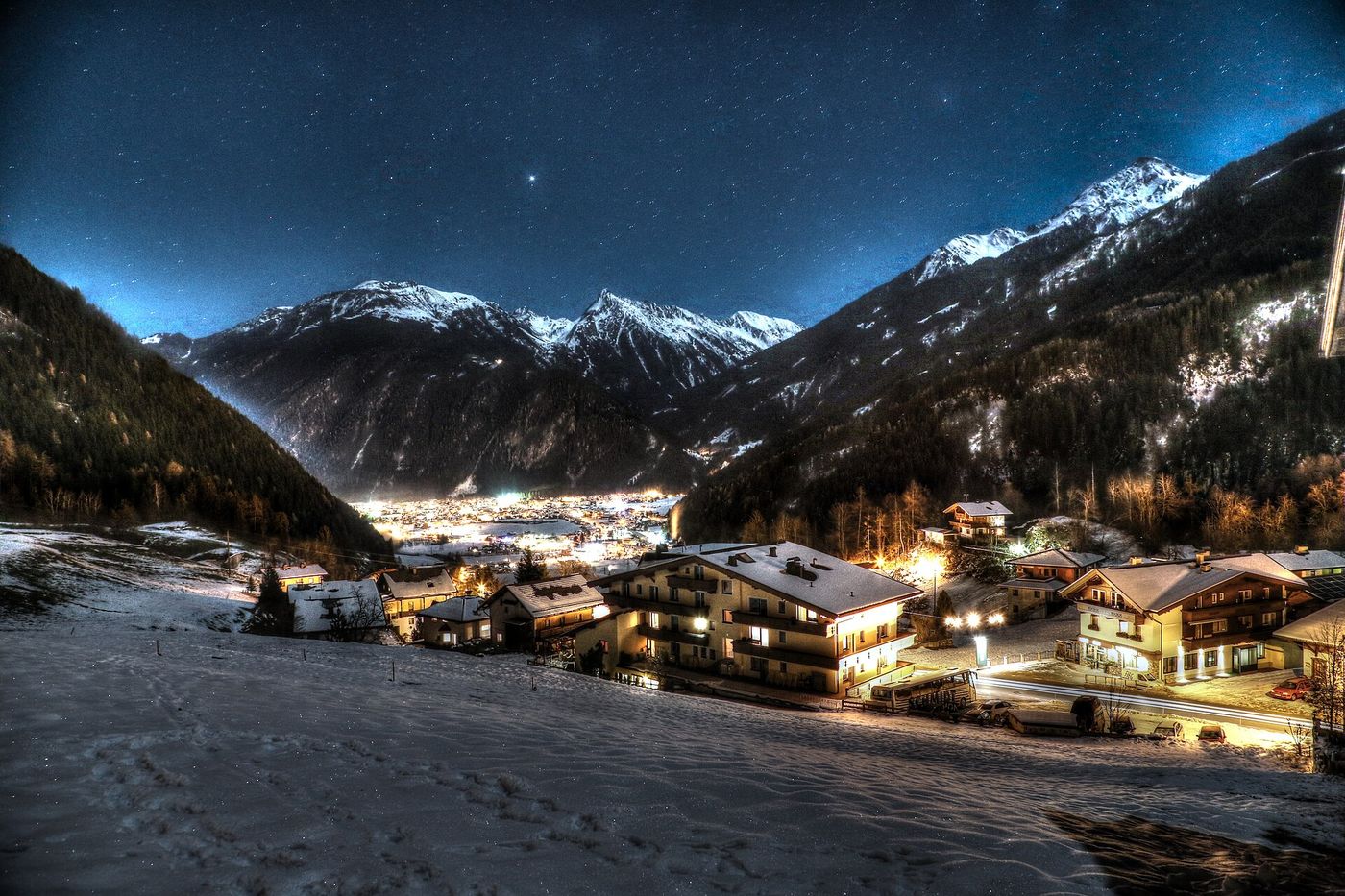 Snow-covered chalets of Mayrhofen lit up at night with the Zillertal valley and mountains behind