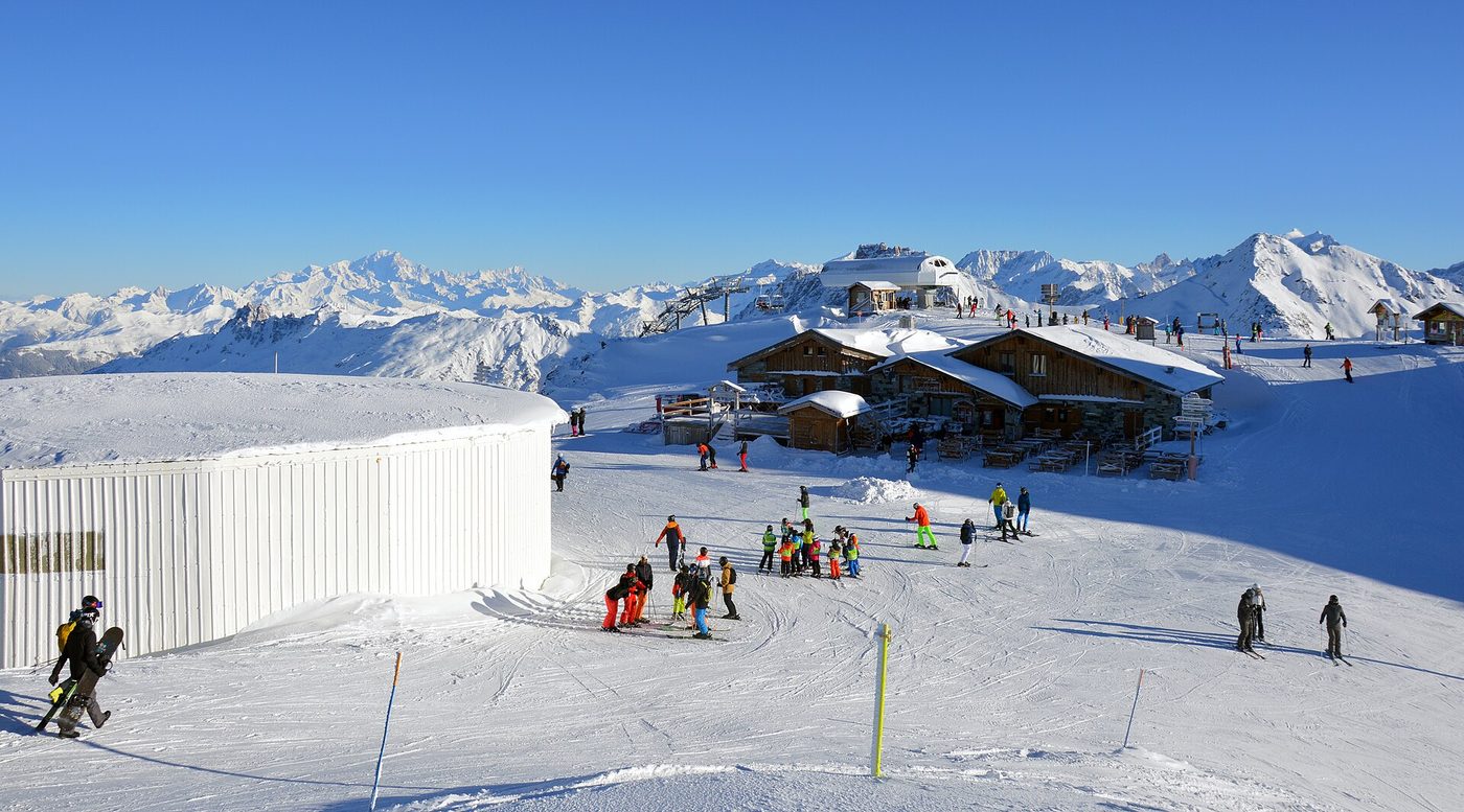 The summit ski area of Mont de la Chambre in the morning sun with mountain huts and the vast 3 Vallées landscape beyond