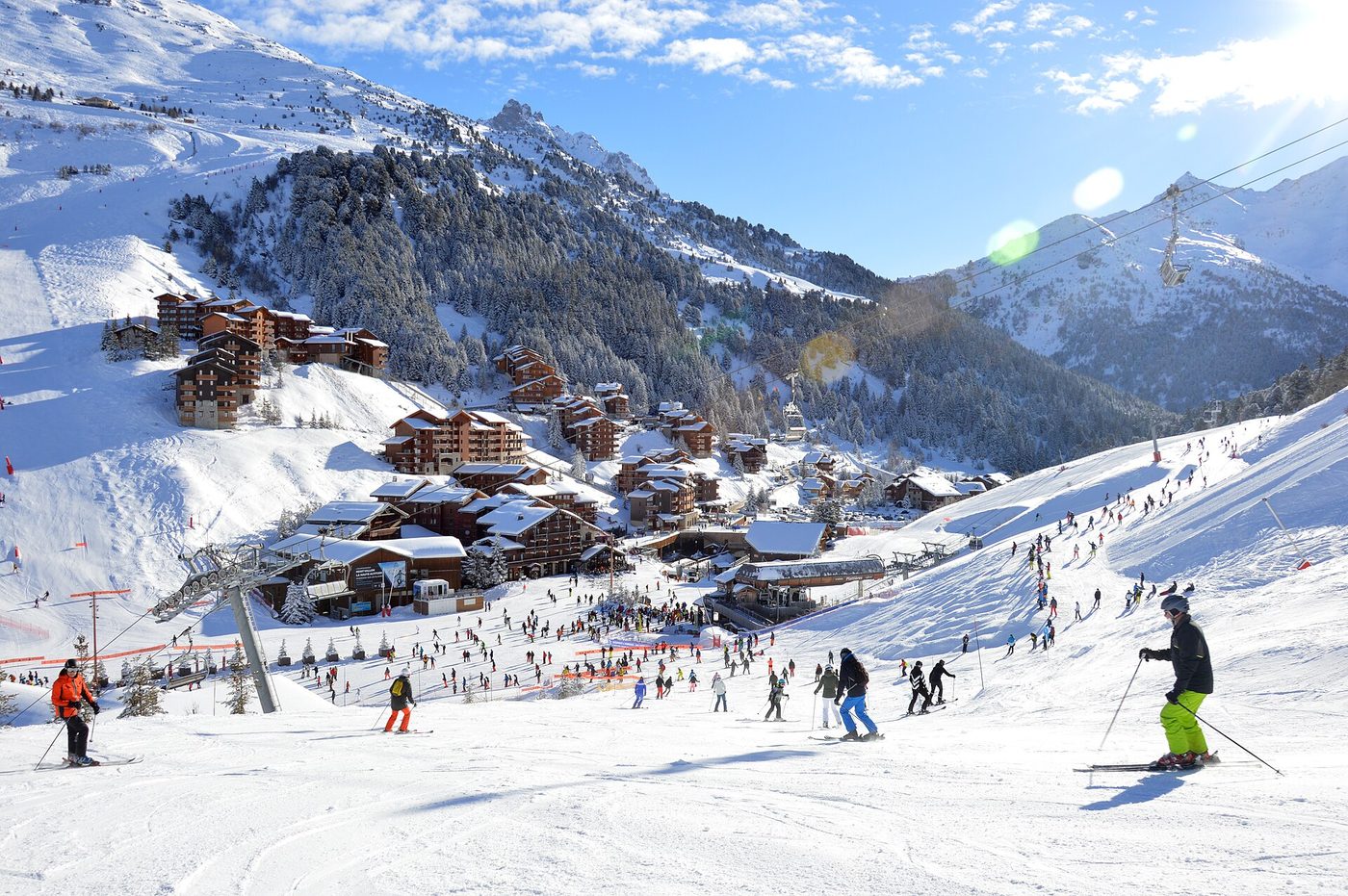 Skiers descending the piste Martre above Méribel-Mottaret with the chalet village and wooded slopes below