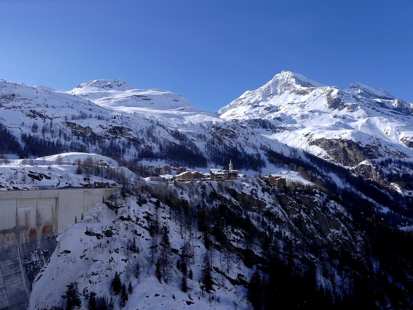 The village of Tignes 1800 set on a hillside beneath snowy peaks, viewed from the Tignes dam in winter