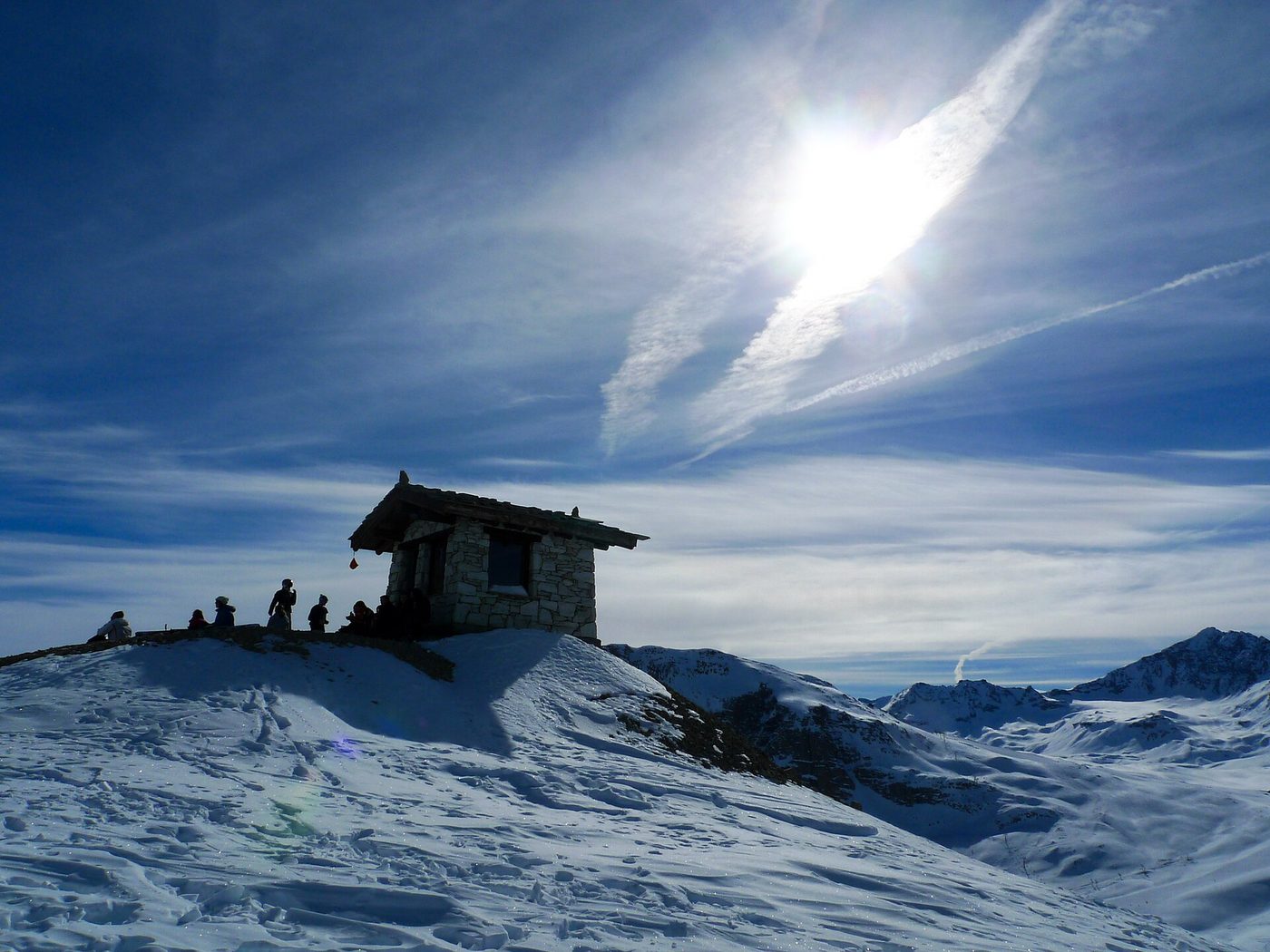 High snowy alpine ridge above Val d'Isère with skiers silhouetted on a summit viewpoint under a bright winter sky