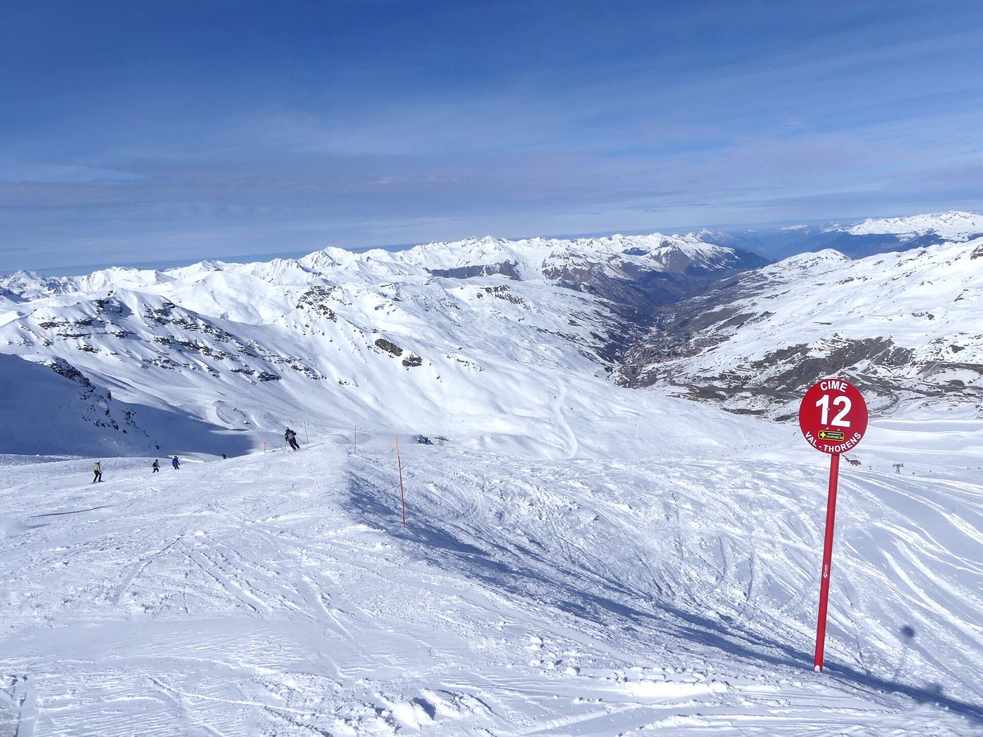Skiers descending a wide red piste at Val Thorens with snow-covered peaks and the Cime de Caron in the background