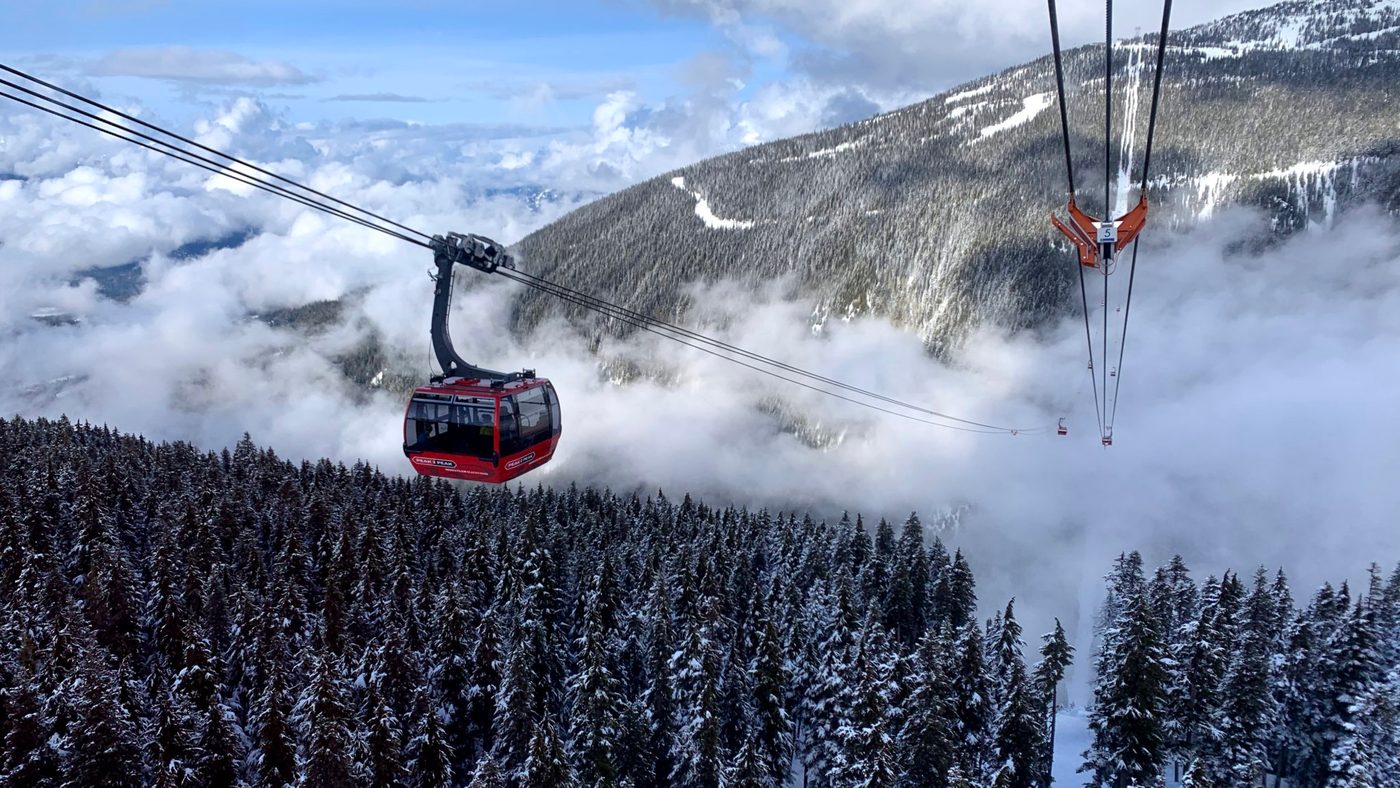 A red PEAK 2 PEAK gondola cabin crossing above the snow-covered forest between Whistler and Blackcomb