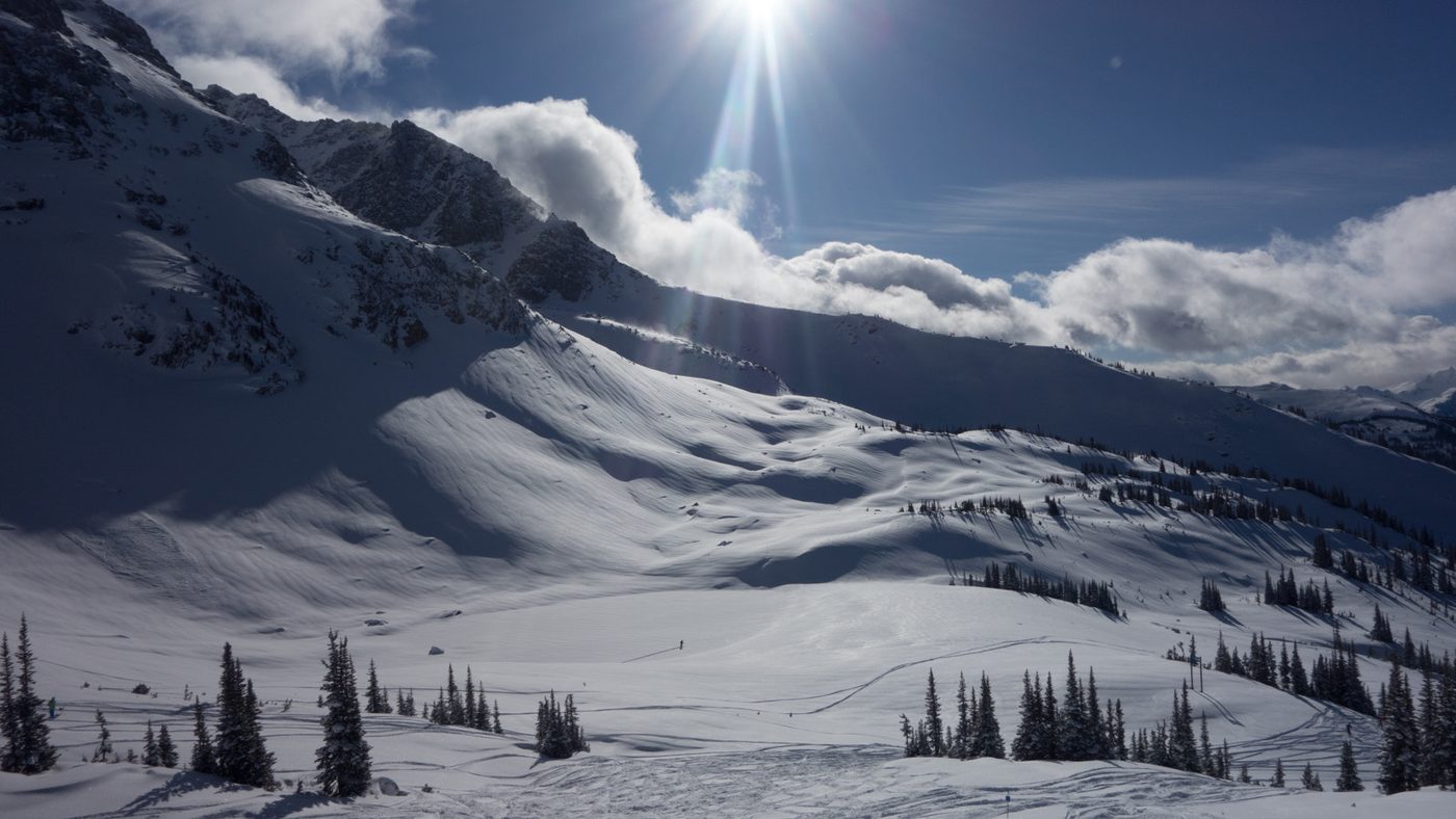 A wide snow-filled alpine bowl on a sunny powder day at Whistler with peaks and snow-laden trees